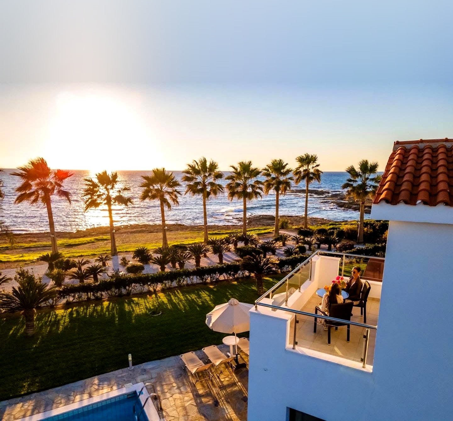 Platzia Beach Villas balcony overlooking palm trees and the sea at sunset